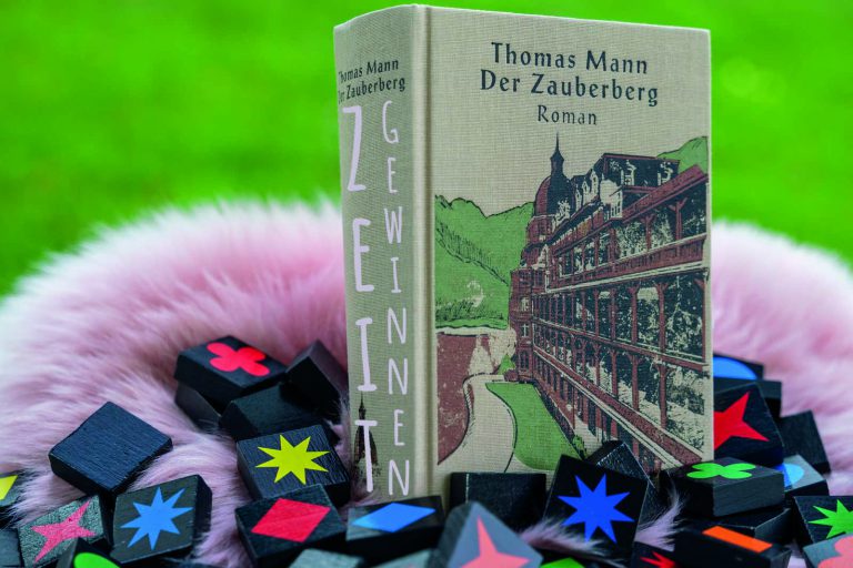 Das Buch Zauberberg von Thomas Mann umrahmt von Spielsteinen mit der Bildaufschrift: Zeit Gewinnen